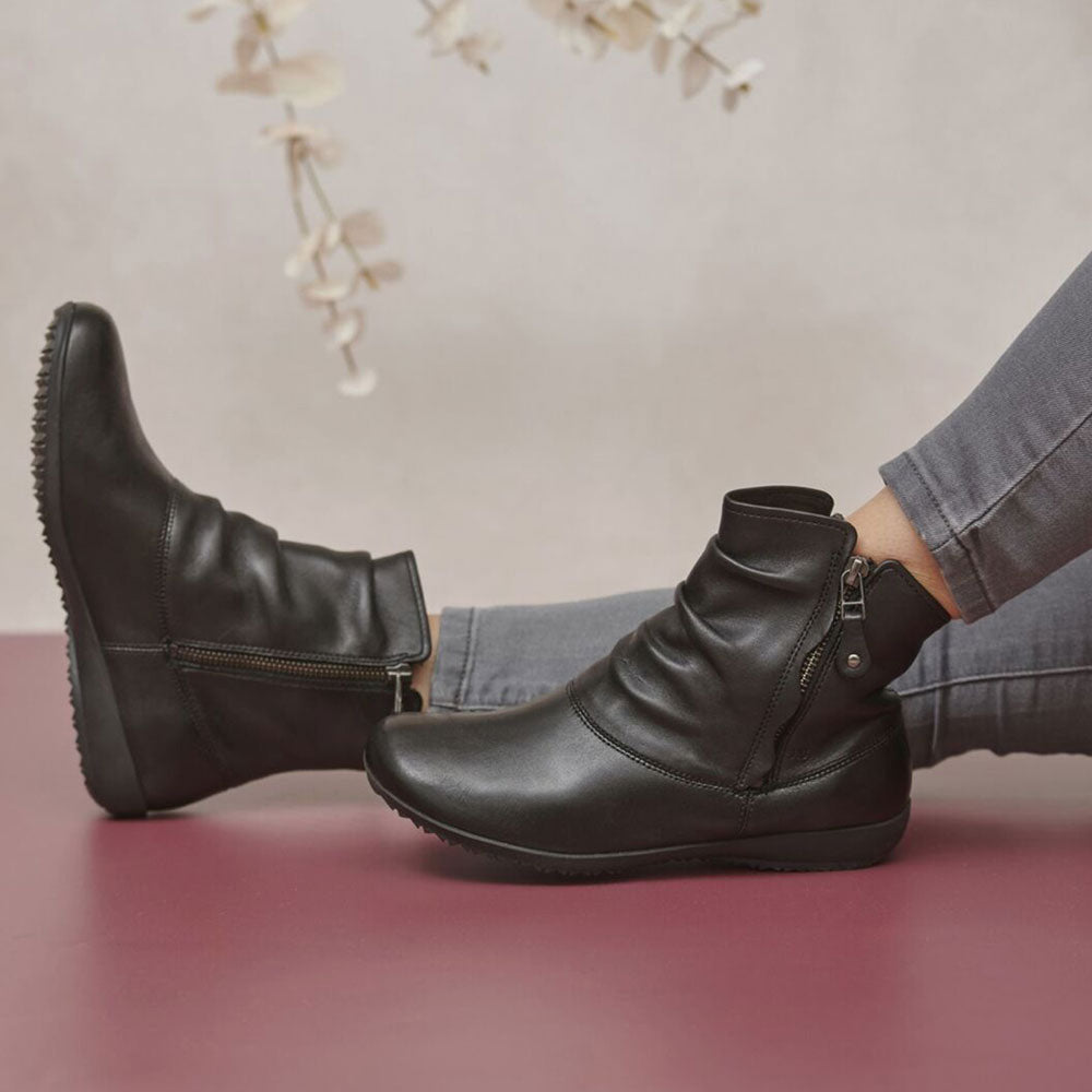 Black leather boots worn with gray pants on a pink surface.