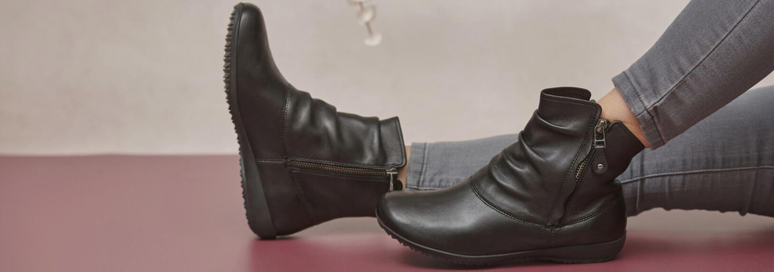 Black leather boots being worn on a pink surface with a neutral background