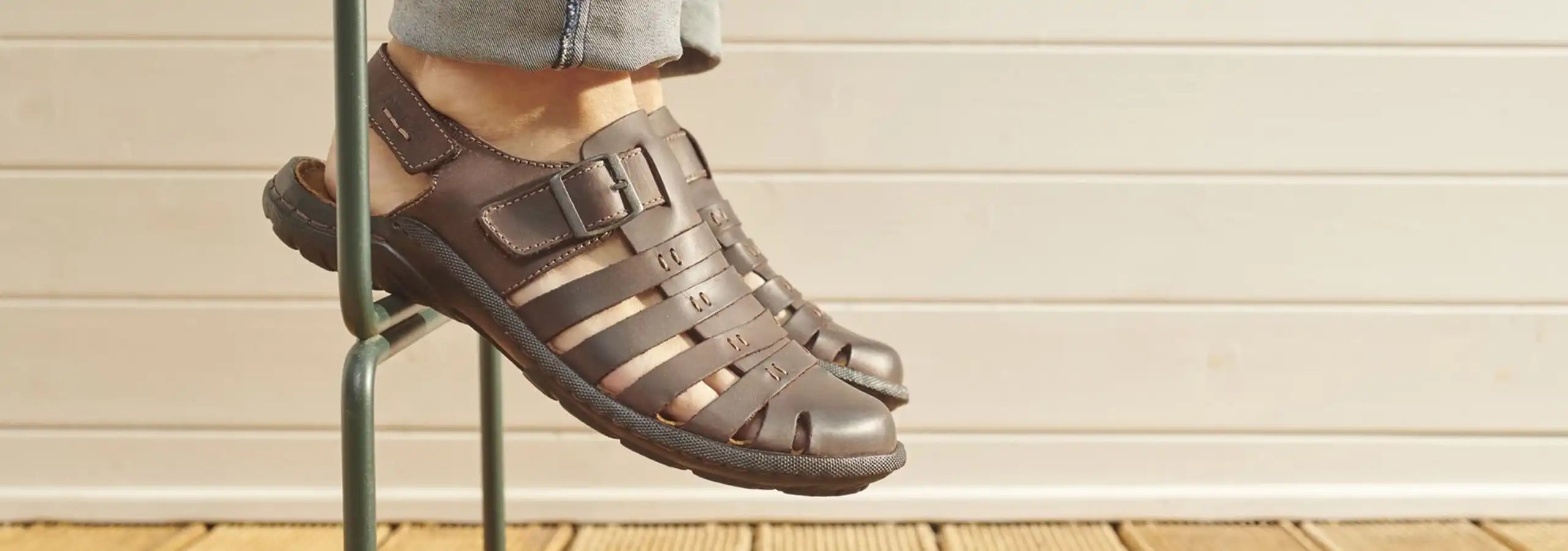 Brown sandals worn with jeans on a wooden floor.