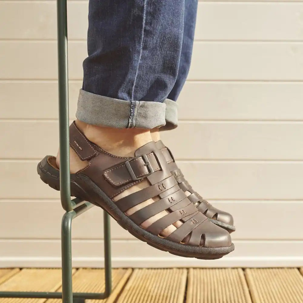Brown sandals worn with rolled-up jeans on a wooden deck.