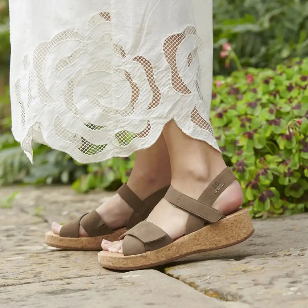 Brown sandals worn with a white lace skirt against a garden background
