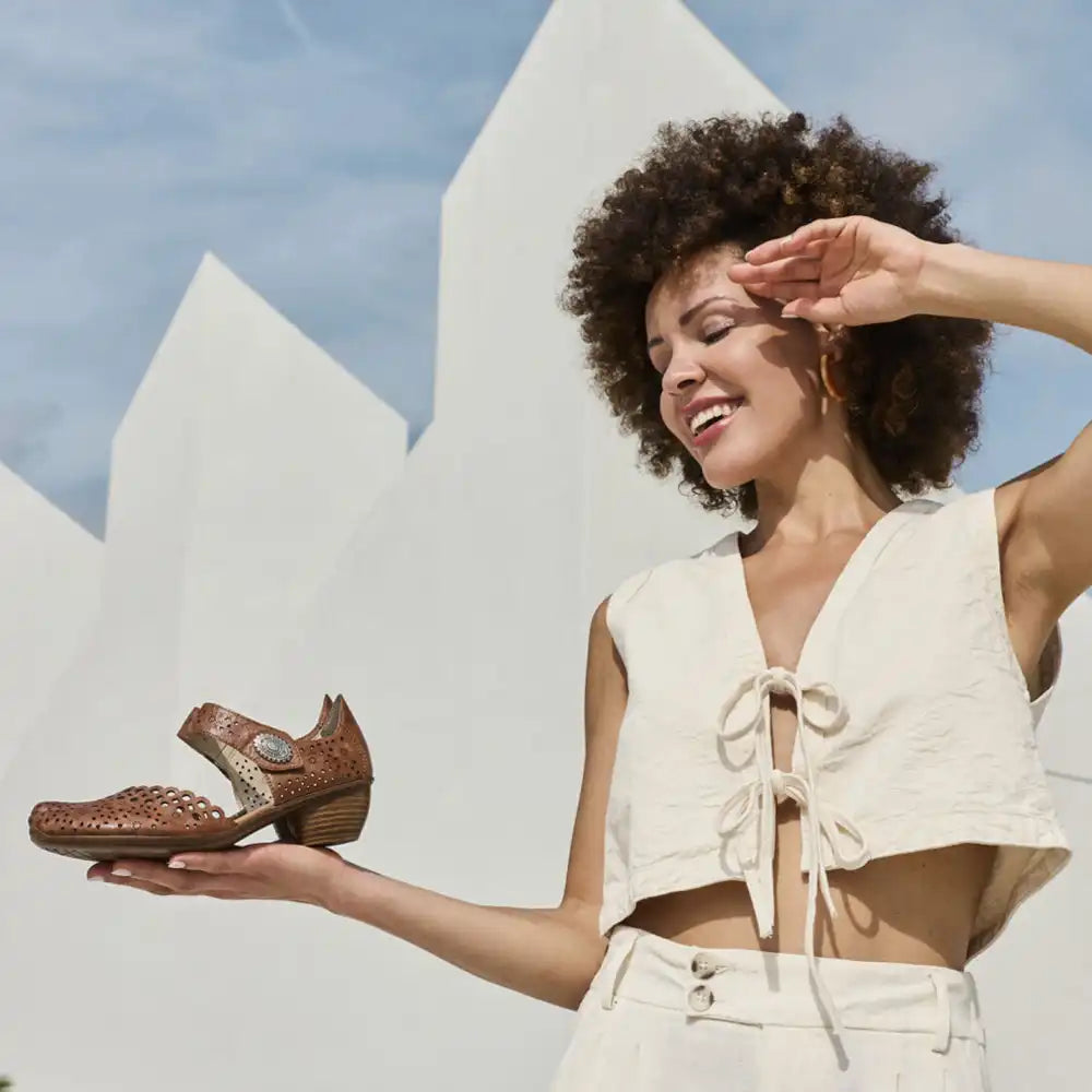 Woman holding a brown sandal against a white architectural background