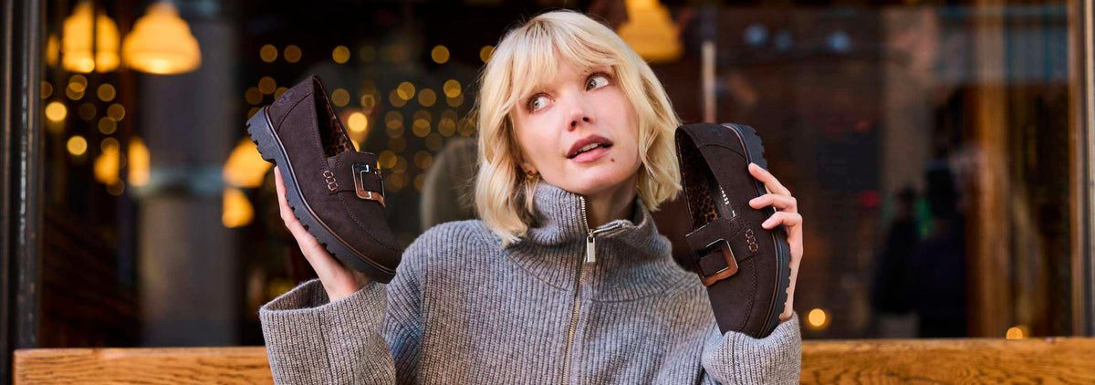 A woman holding up a pair of brown autumn winter shoes